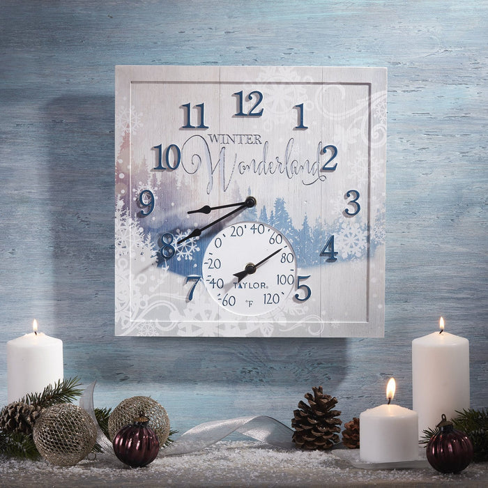 Square Winter Wonderland clock with built in thermometer mounted on a frosty blue wall beside candles and pine ornaments