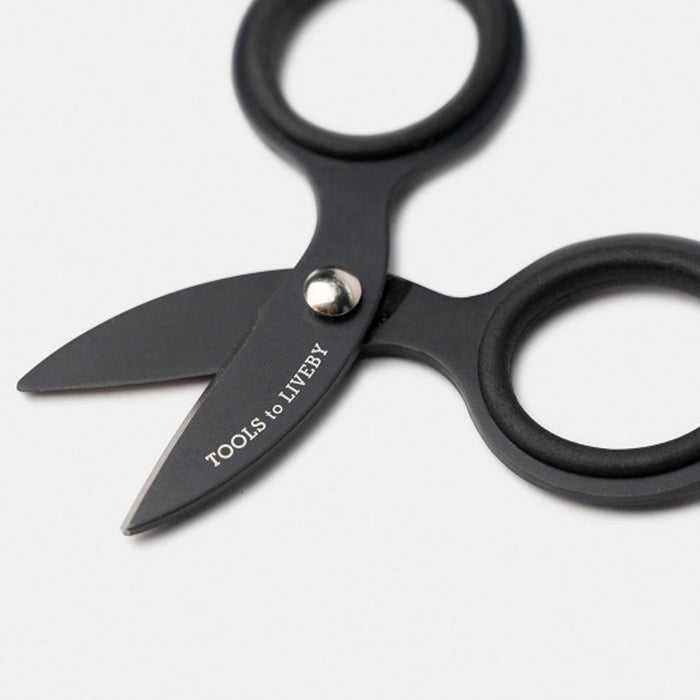 Close up of small black steel scissors with 'Tools to Liveby' branding on blade on white surface
