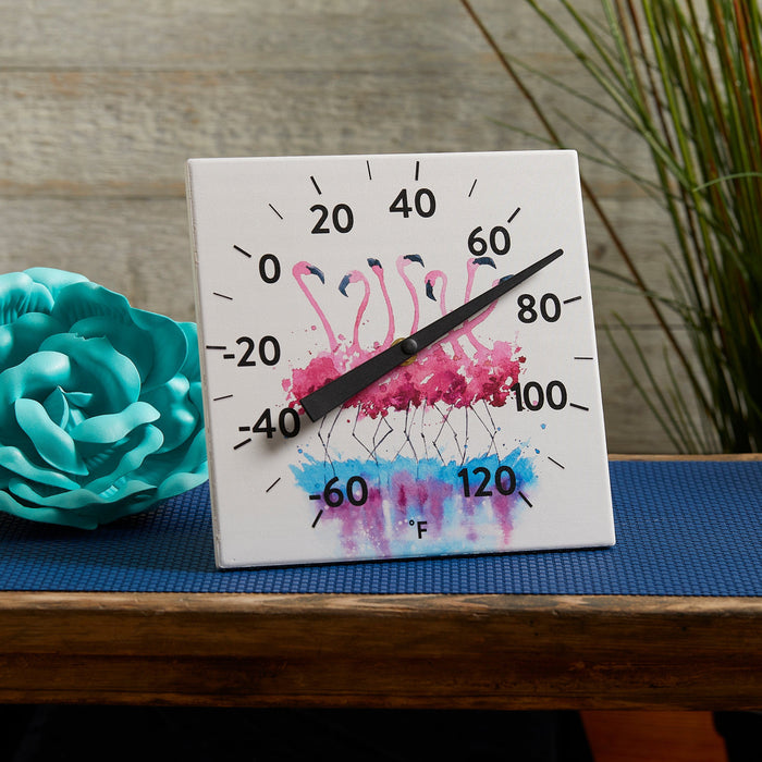 Ceramic Flamingo thermometer set against a wooden fence with turquoise paper flower and blue garden backdrop