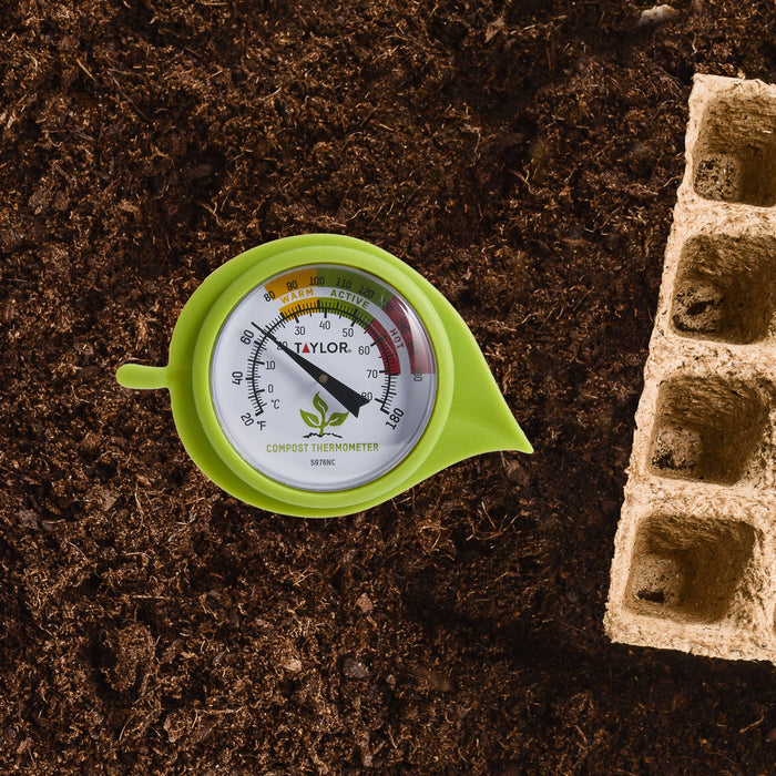 Soil bed close up showing dark mulch and brick edging with a green compost thermometer partially visible.
