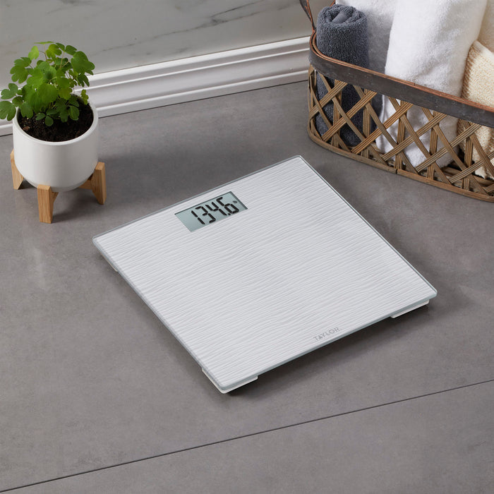 Digital bathroom scale on the floor beside a potted plant and a wicker basket with towels