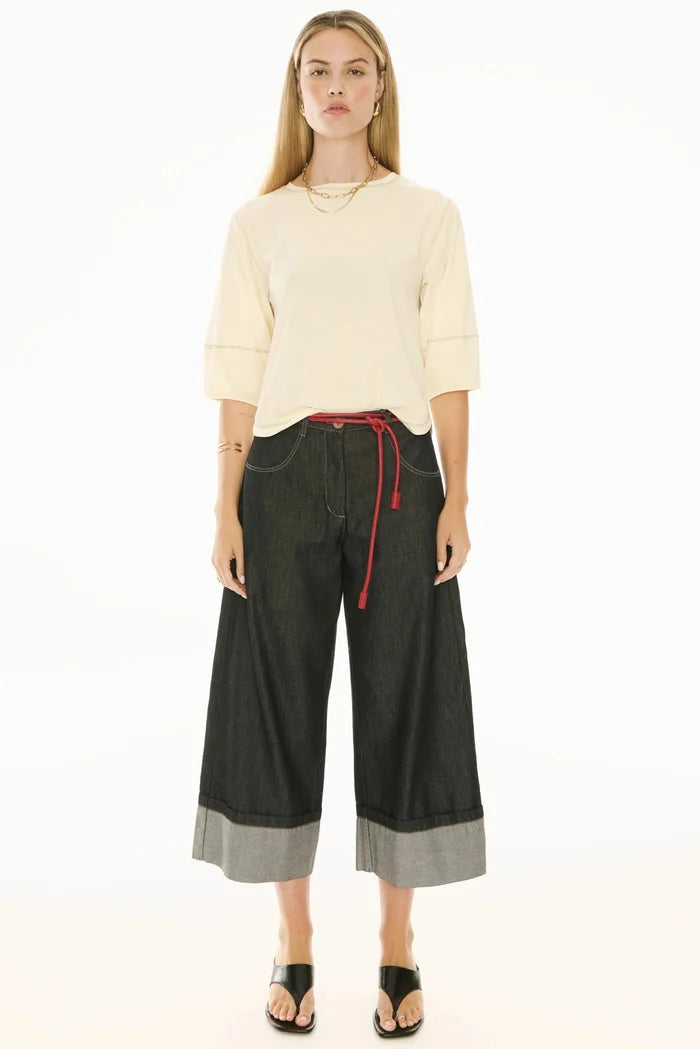 Woman wearing a cream sweater and black wide-leg pants with red drawstring on a white background