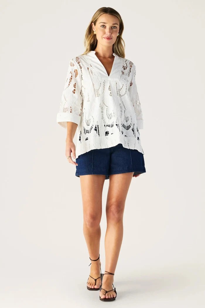 Woman wearing a white lace top and navy shorts on a white background