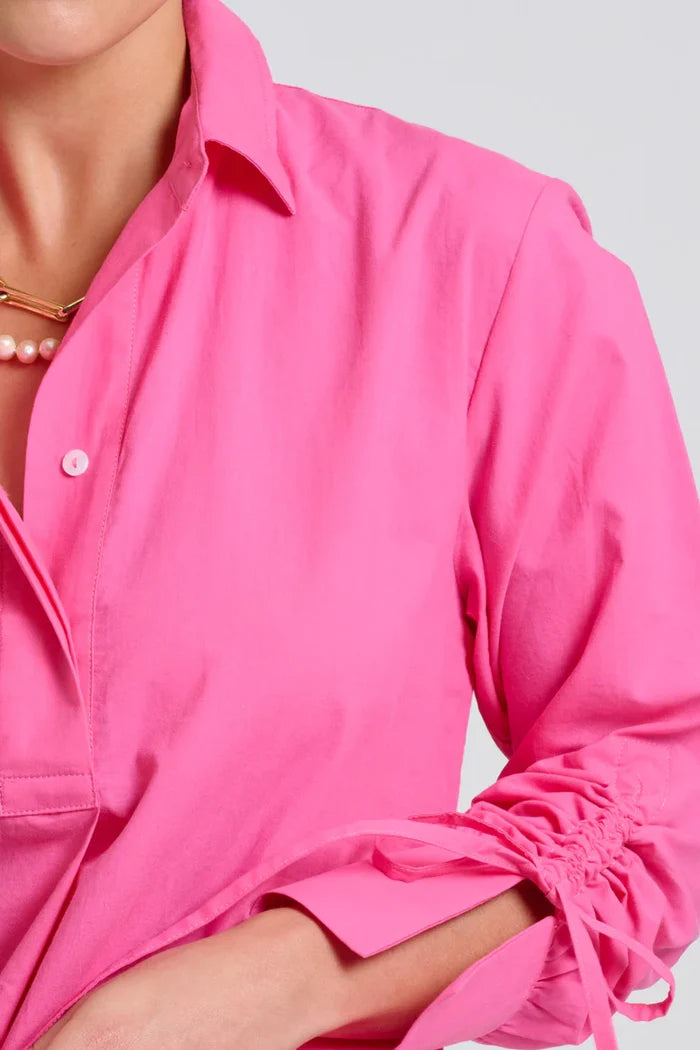 Close-up of a person wearing a bright pink shirt with rolled-up sleeves on a light gray background.
