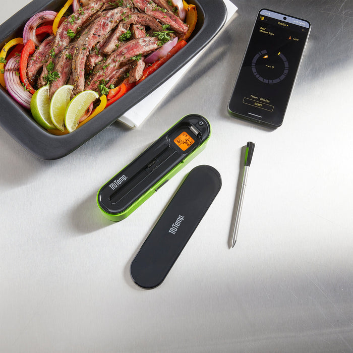 Beef roast with onions and peppers cooking in a pan beside a smartphone displaying the TruTemp app and a thermometer probe