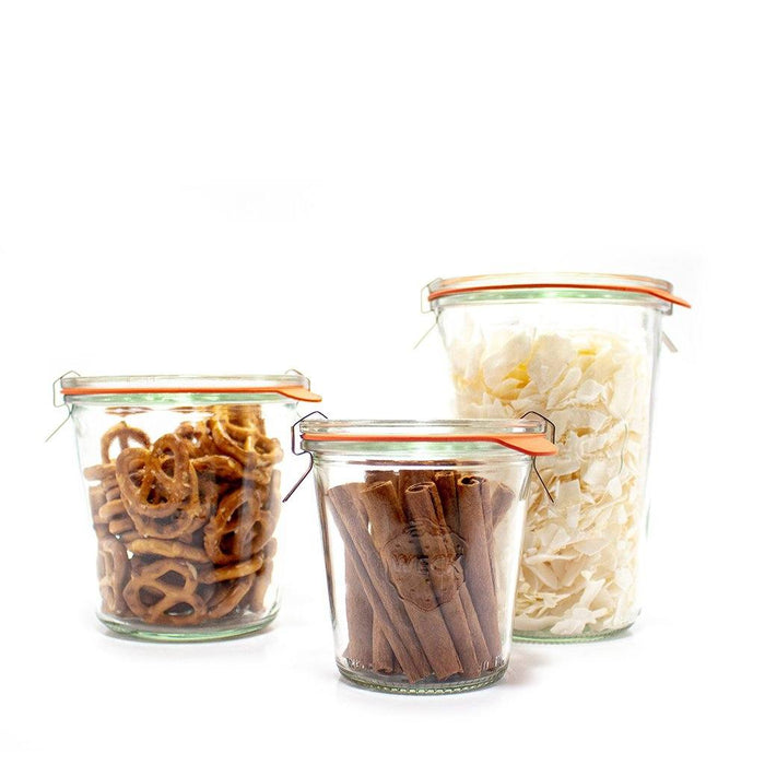 Set of three glass Weck Mold Jars with glass lids and clamps holding pantry snacks on white background