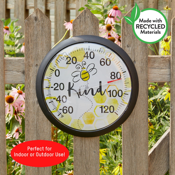 Bee Kind thermometer mounted outdoors against a wooden fence with a recycled materials badge visible.