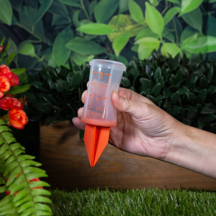 Hand holds orange 2 inch silicone sprinkler gauge with orange markings.