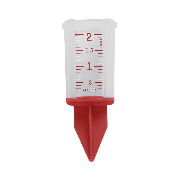 Hand holding a 2 inch silicone sprinkler gauge with red markings in a garden background.