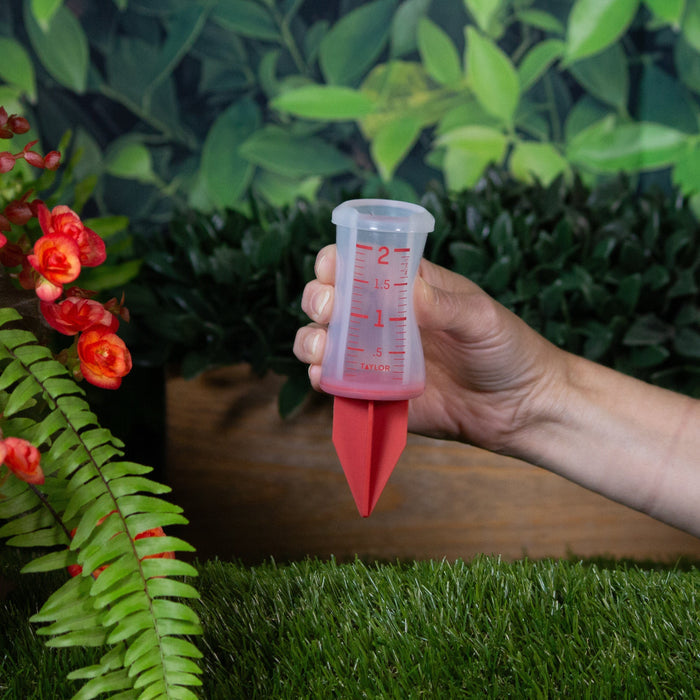 Red 2 inch silicone sprinkler gauge held in hand outdoors among plants