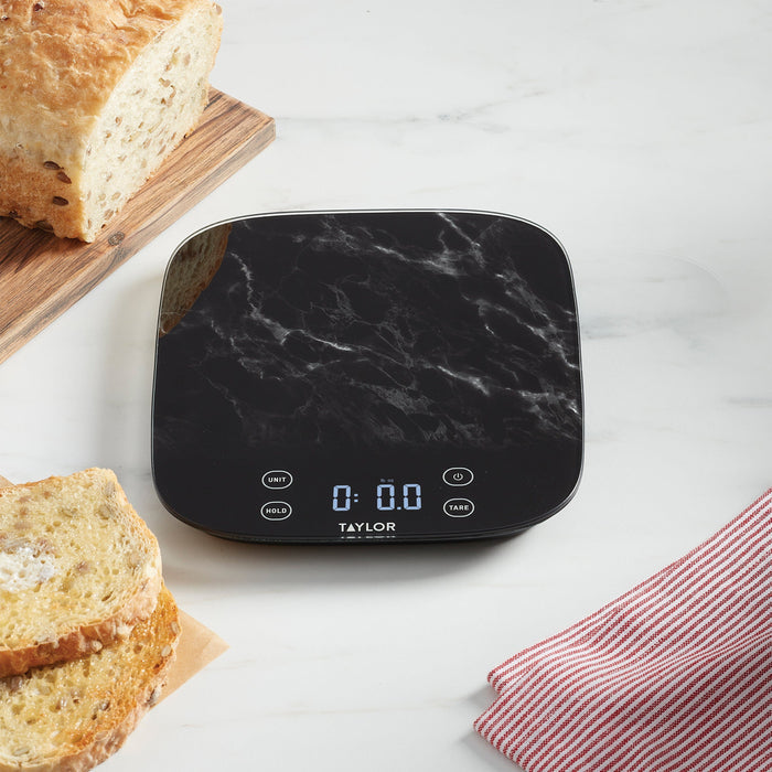 Loaf of bread on cutting board beside the black marble digital kitchen scale