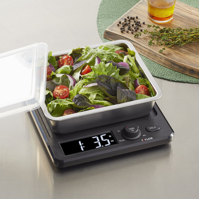 Salad in a stainless tray on a digital kitchen scale with a wooden board and oil bottle in the background