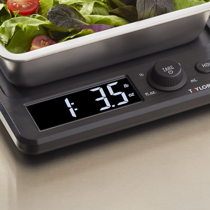 Close-up of mixed greens and cherry tomatoes in a stainless tray on the kitchen scale
