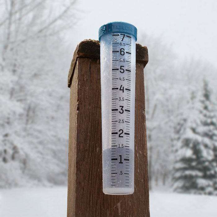 Close up of a 7 inch silicone rain gauge mounted on a wooden post in a snowy yard