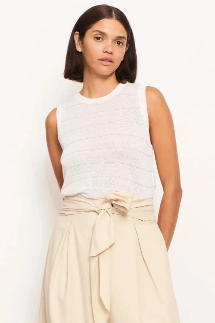 A female model wearing a white sleeveless top with ribbed detailing and a matching skirt.