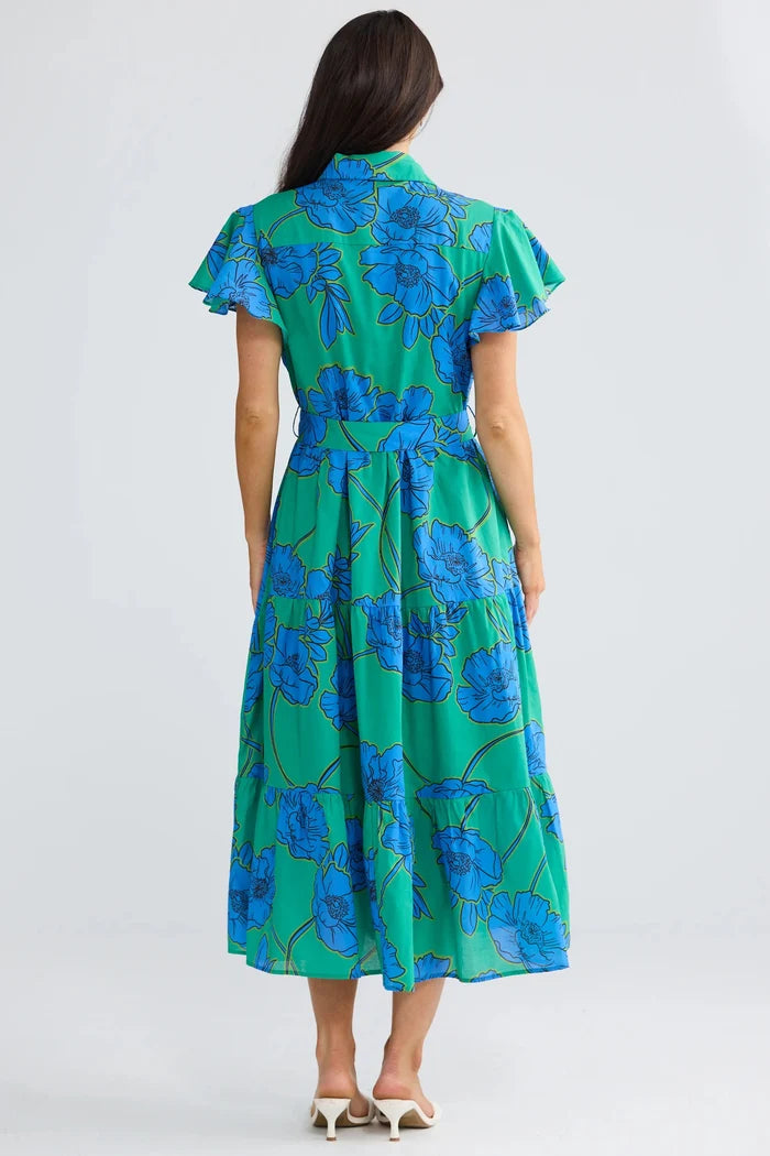 A woman viewed from behind wearing a green midi dress with a blue floral print, short flutter sleeves, and a matching waist tie, set against a plain light gray studio background.