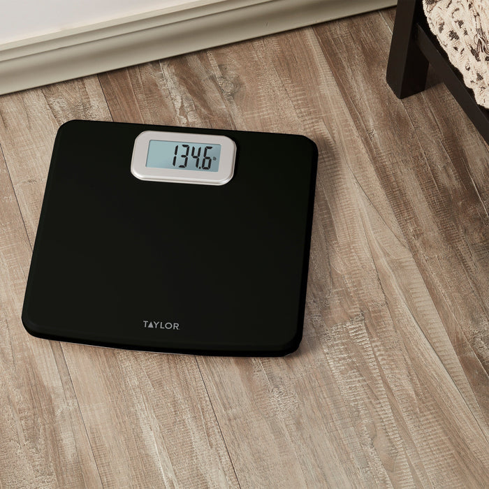Black antimicrobial digital scale on wood floor with the display reading 134.6 lb