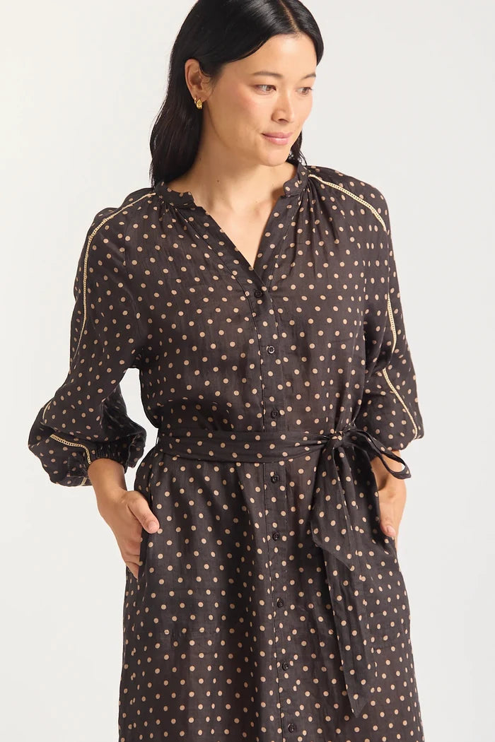 Woman wearing a black dress with gold polka dots on a white background