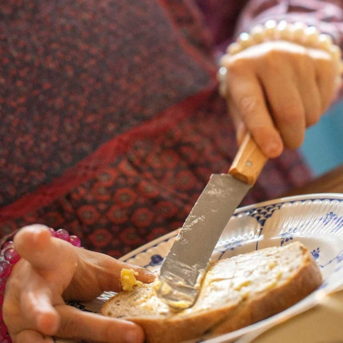 Person spreading butter on a slice of bread with an Opinel brunch knife.
