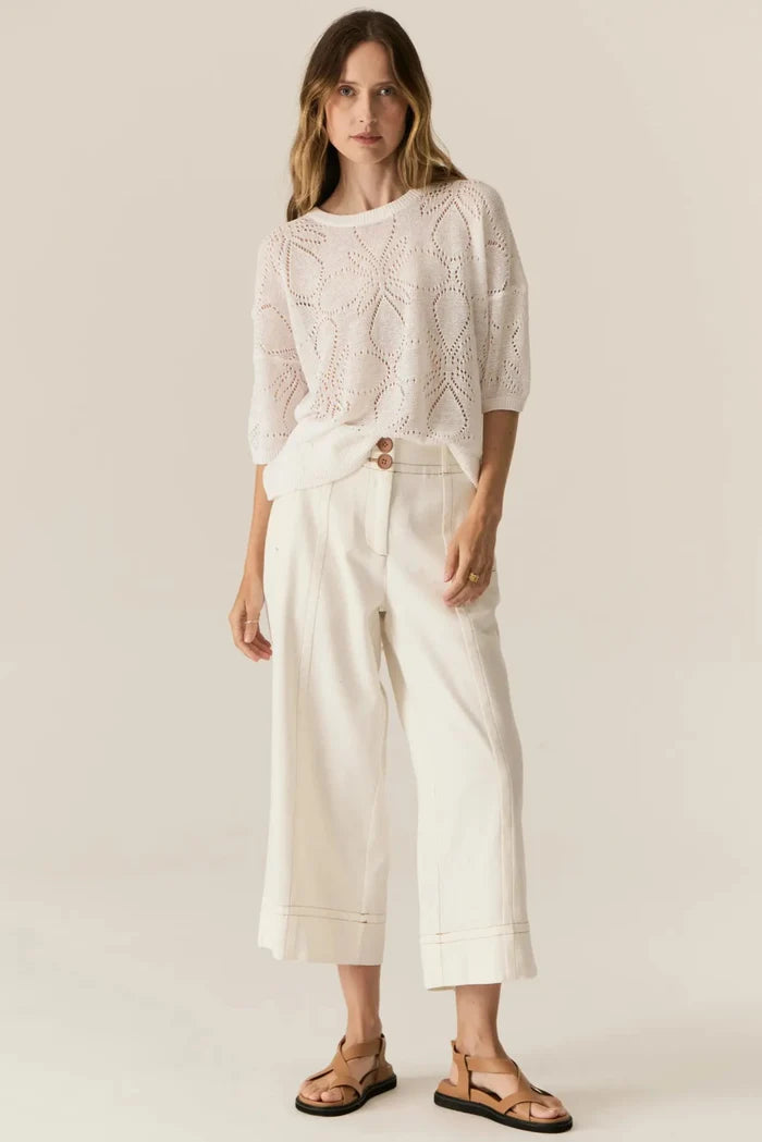 Woman wearing a white lace top and wide-leg pants against a plain background