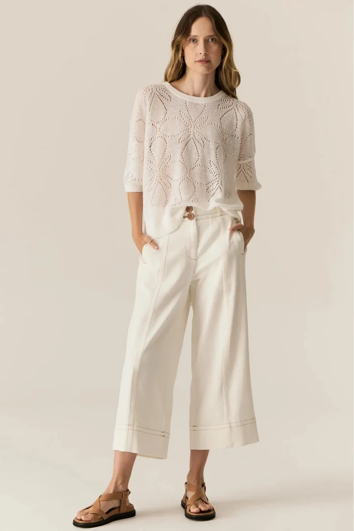 Woman wearing a white lace top and wide-leg pants against a plain background