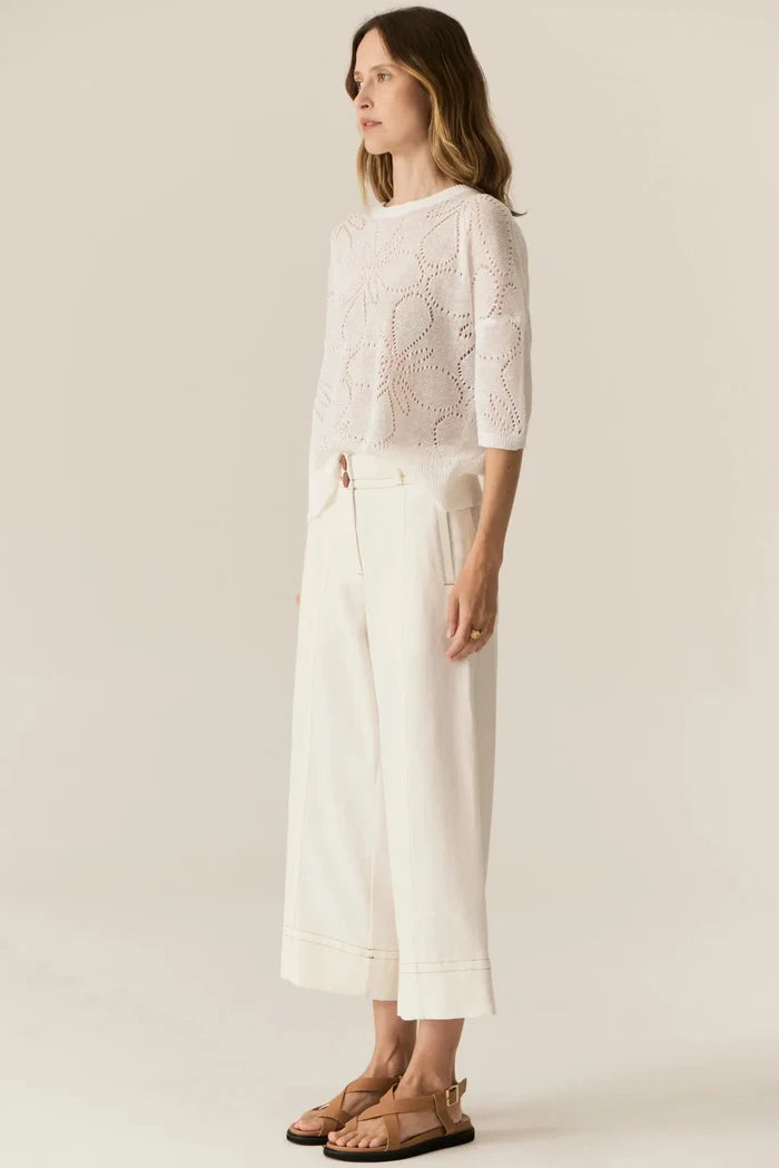 Woman wearing a white lace top and wide-leg pants against a plain background