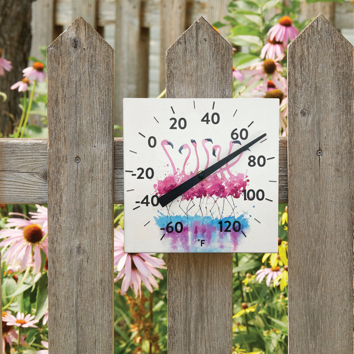 Ceramic Flamingo thermometer displayed outdoors against a weathered wooden fence with a garden in the background