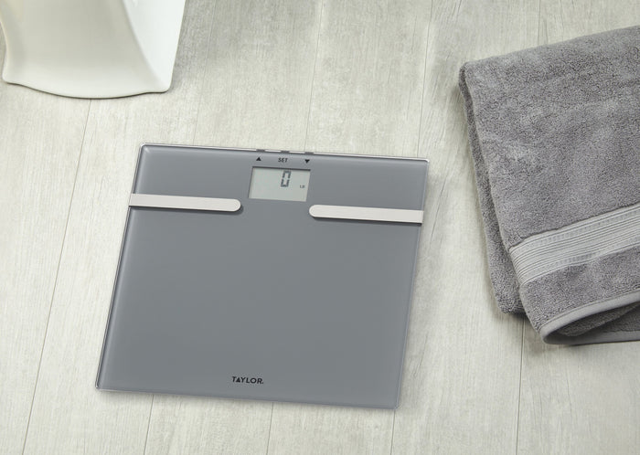 Charcoal grey body composition scale with two white bars across the surface on a light wood floor and Taylor logo