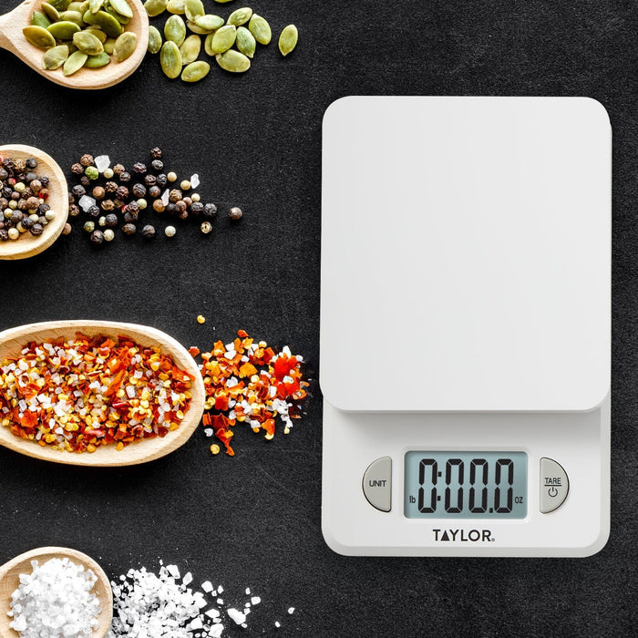 Taylor compact digital kitchen scale on a dark surface with bowls of seeds and salt nearby