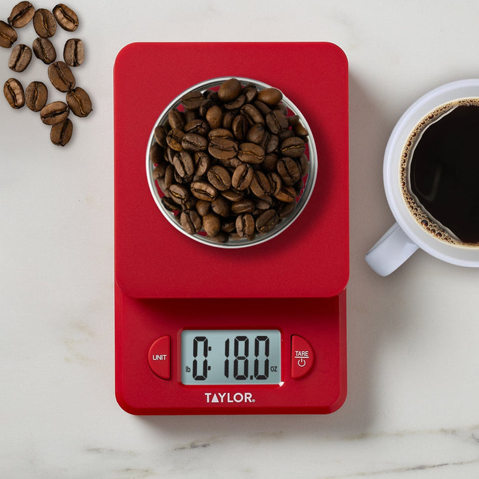 Red compact digital kitchen scale with a metal bowl filled with coffee beans and scattered beans nearby