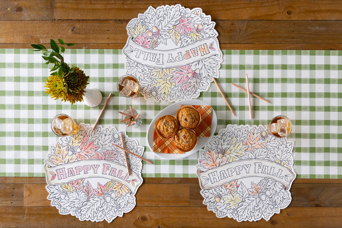 Tablescape with three Die-cut Happy Fall Coloring Placemats on top of a green check table runner with color pencils laid out with flowers and snacks.
