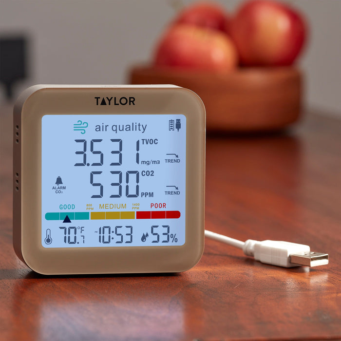 Taylor digital air quality monitor with USB power cord and plug coiled beside it on a wooden desk