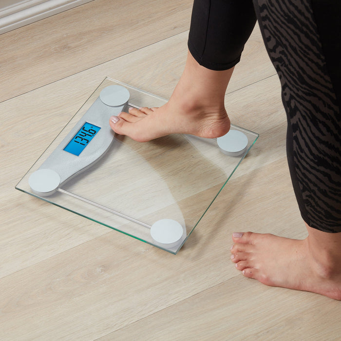 Bare foot on a digital glass bathroom scale with a blue display on a wood floor
