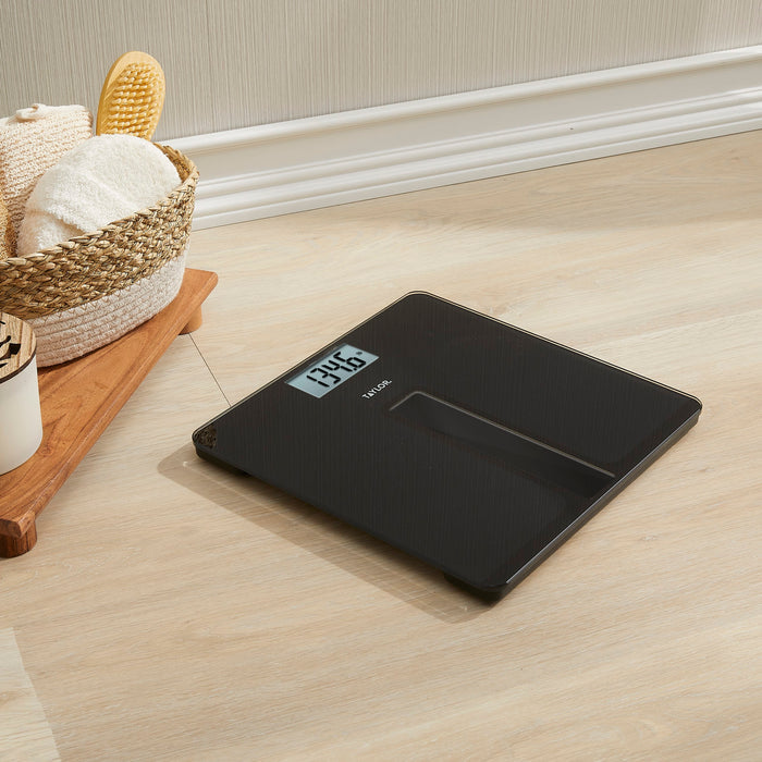Digital light powered bath scale on a wooden floor beside a basket of towels