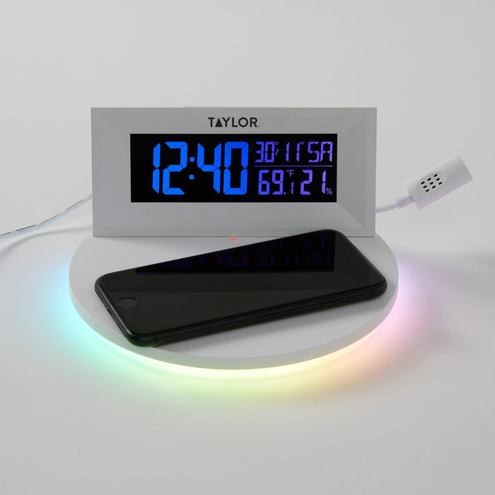 White mood light weather station with a smartphone on the wireless charging pad and vivid blue display