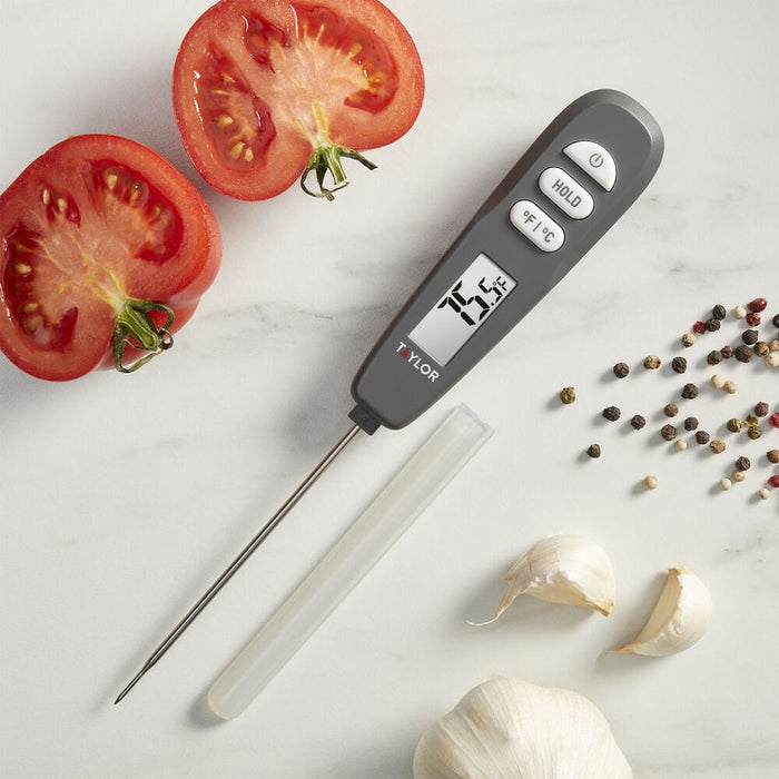 Digital Rapid Response Thermometer beside halved tomatoes garlic and peppercorns on a white marble surface