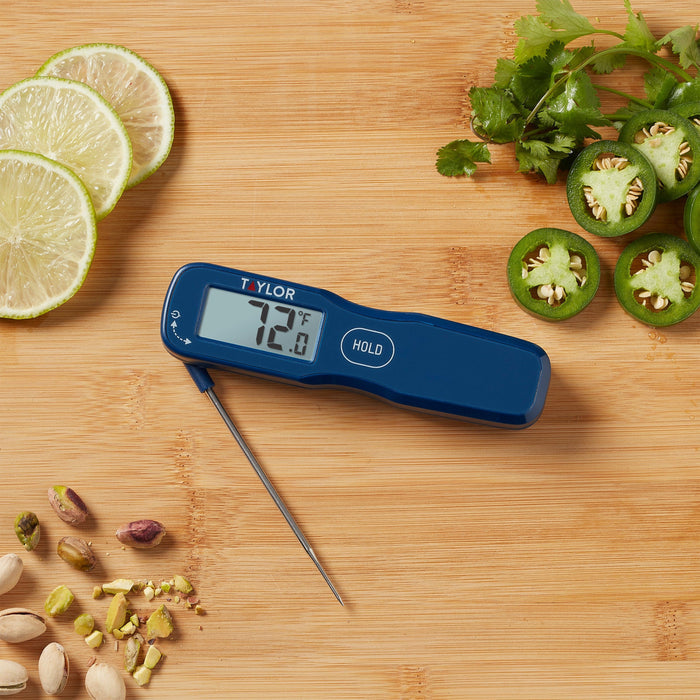 Blue digital thermometer with metal probe on a wooden cutting board beside lime slices cilantro and jalapeño slices.