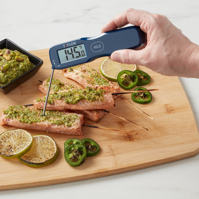 Blue waterproof digital thermocouple thermometer with probe inserted into seasoned salmon fillets on a wooden cutting board with lime wedges and jalapeños.