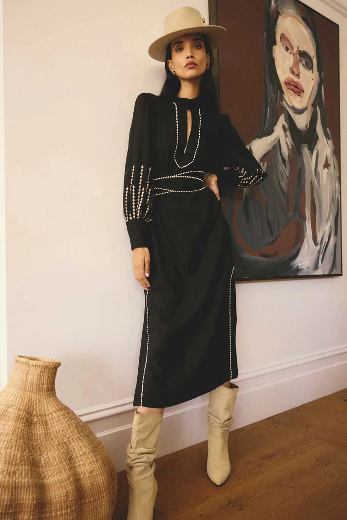 Woman in a black outfit with white accents standing in a room with a painting on the wall.