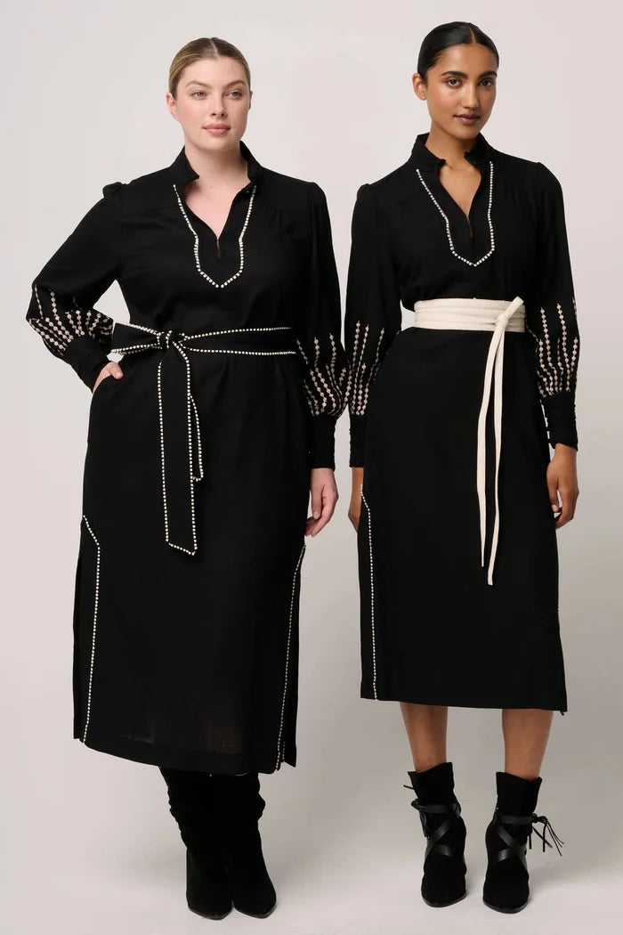 Two women wearing black dresses with decorative elements on a plain background