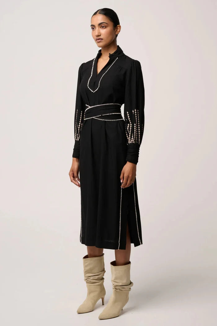Woman wearing a black dress with decorative elements and beige boots on a white background