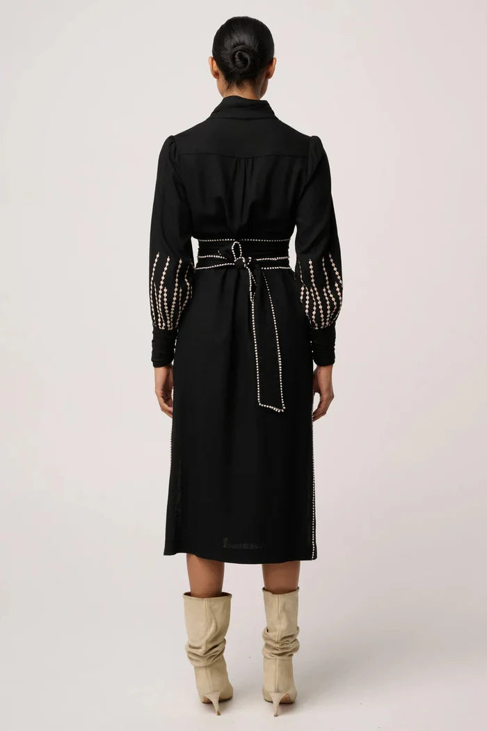 Person wearing a black dress with studded details on a white background