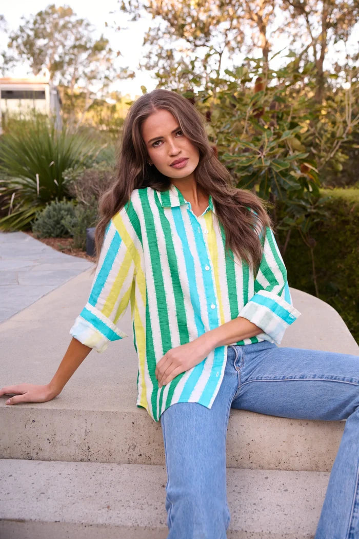 Woman wearing a striped shirt and jeans sitting on steps outdoors.
