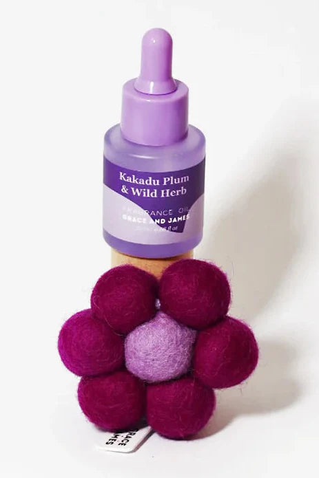 Purple fragranced oil bottle with dropper and purple and pink flower shaped felt air freshener on a white background