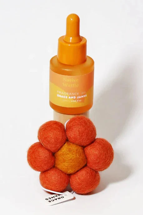 Orange fragranced oil bottle with dropper and flower shaped felt air freshener on a white background
