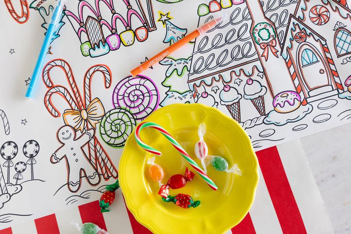 Yellow bowl with candy canes and gumdrops on a table with a paper coloring runner featuring gingerbread houses and candy-themed illustrations that are partially colored in.