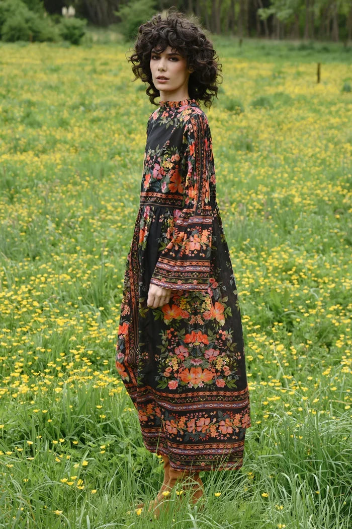 Woman in a floral dress standing in a field of yellow flowers