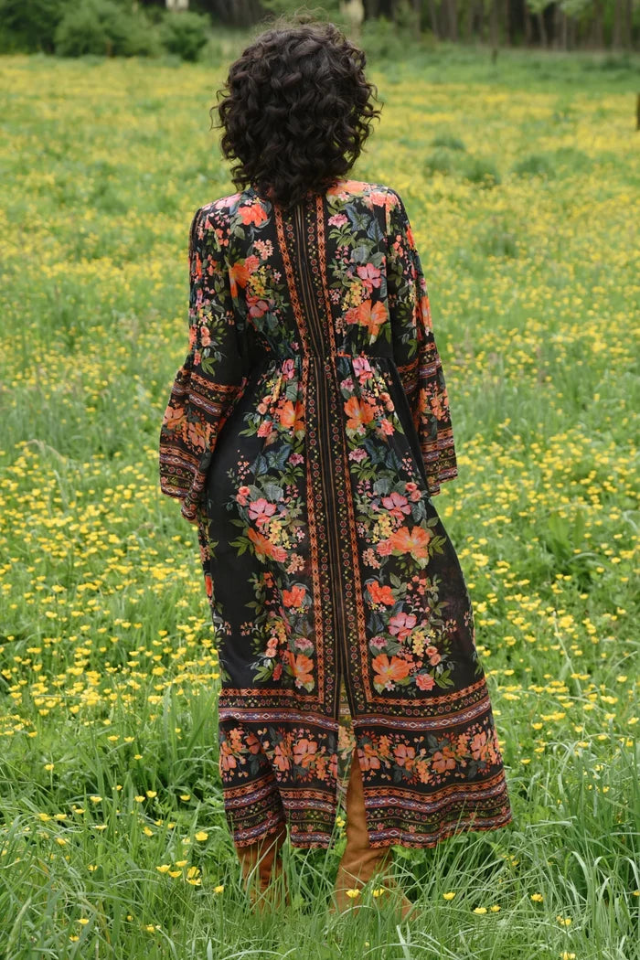 Person wearing a floral dress standing in a field of yellow flowers.