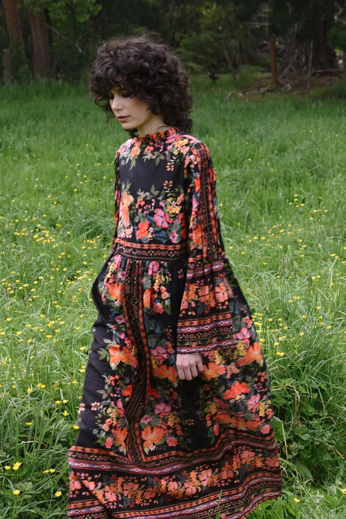 Woman in a floral dress standing in a grassy field with wildflowers.