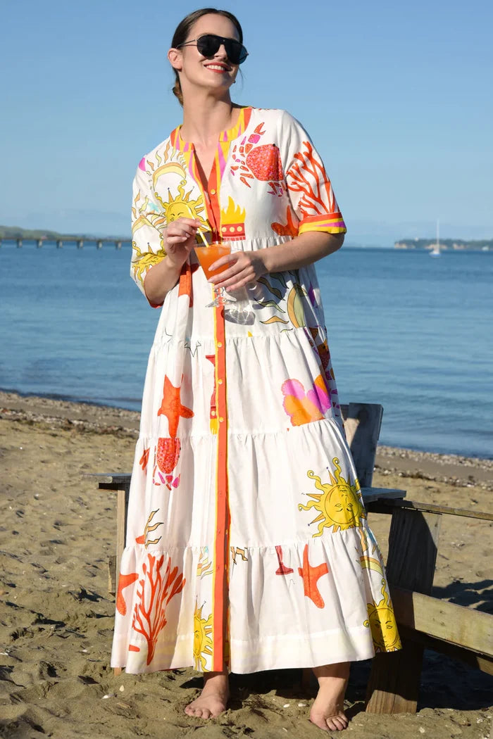 Woman in a colorful dress with floral patterns standing on a beach.